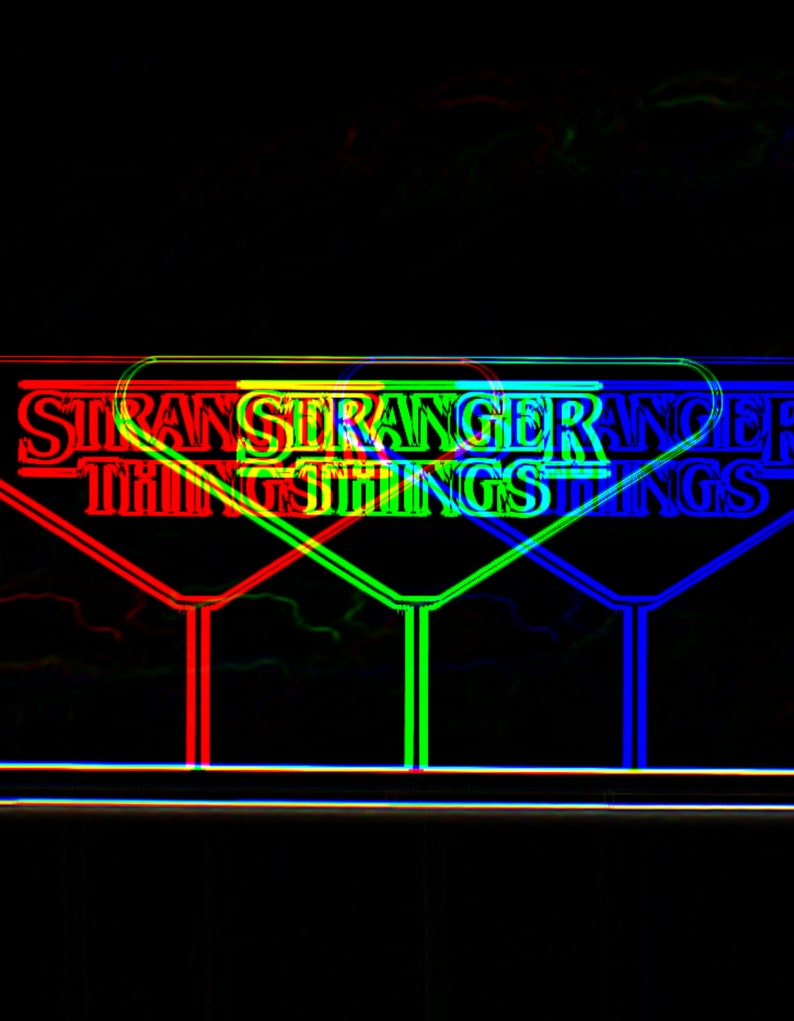 Pode incluir: Uma placa de n&eacute;on com as palavras "Stranger Things" em vermelho, verde e azul. A placa tem a forma de um tri&acirc;ngulo.