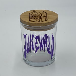 May include: A clear glass jar with a wooden lid. The jar has the word "JUICEWRLD" in purple lettering. The lid is engraved with a carton design and the words "JUICE WRLD LEGEND 999".