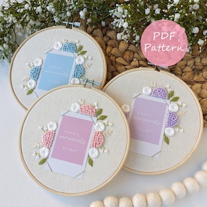 May include: Three embroidered hoops with floral designs. Each hoop features a central card with the text "Happy Moments" and the dimensions "2x3". The embroidery includes blue, pink, and purple flowers, white buttons, and green leaves.