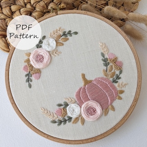 May include: Embroidered hoop art featuring a pink pumpkin with white and pink flowers and greenery. The text "PDF Pattern" is in the upper left corner of the image.