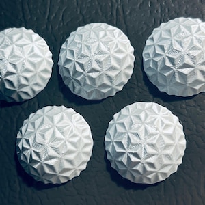 May include: Five white, spherical objects with a geometric, star-like pattern across their surface. The objects are arranged on a dark, textured background. The design features a series of interconnected, triangular shapes.