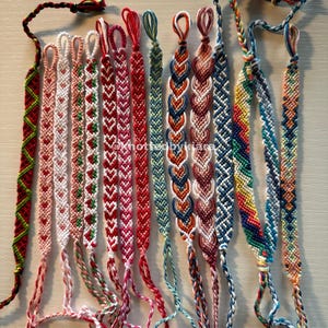 Puede incluir: Una colección de 18 pulseras de amistad coloridas con varios patrones, incluyendo corazones, chevron y diseños en zigzag. Las pulseras están hechas con hilo de bordar y tienen borlas en los extremos.
