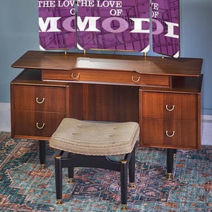May include: A vintage vanity set with a three-panel mirror featuring the text "FOR THE LOVE OF MOD". The vanity has a wooden top and drawers with gold handles. A matching stool with a patterned cushion sits in front of the vanity.