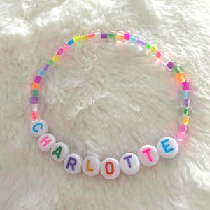May include: A bracelet made of colourful beads, spelling the name "CHARLOTTE" in white letter beads. The bracelet features a variety of small, translucent beads in shades of pink, green, yellow, and blue.