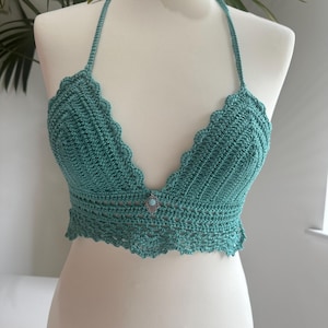 Pode incluir: Um top halter de crochê turquesa com um amuleto de prata decorativo com uma pedra turquesa.