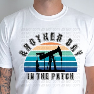 May include: White t-shirt featuring a vintage-style sunset graphic and a silhouette of an oil rig. The text "Another Day in the Patch" is printed in black on the shirt.