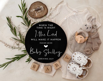 May include: A black and white round sign with the text "WHEN THE TIME IS RIGHT 1. the Lord WILL MAKE IT HAPPEN ISAIAH 60:22 Baby Shelley ARRIVING JULY".  The sign is surrounded by a white knitted baby outfit, a wooden toy, a pair of white baby shoes, and a small wooden sign with the text "coming soon".