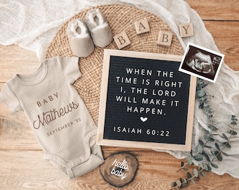 May include: A tan baby onesie with the text "BABY Mathews SEPTEMBER '22" printed on it. A letter board with the text "WHEN THE TIME IS RIGHT I, THE LORD WILL MAKE IT HAPPEN. ISAIAH 60:22" is on a wooden surface. There are wooden blocks that spell out "BABY" and a small wooden sign with the text "hello baby".