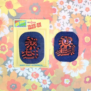 May include: Two iron-on patches featuring a cartoon tiger with orange and black stripes. The patches are on a blue background and have the text "Iron-On" on a white background. The text "Quick - Easy - Economical" is also on the white background.