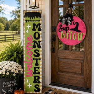 May include: A tall rectangular green sign with black hair detail and the text "welcome MONSTERS" in pink and black, paired with a round pink sign featuring a black witch hat and the text "sup WITCH" with a black and white striped bow.