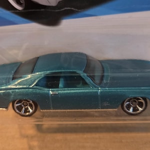 May include: A teal-colored die-cast model car in a clear plastic package. The classic car has a sleek design with chrome wheels. The toy car is a collectible item.