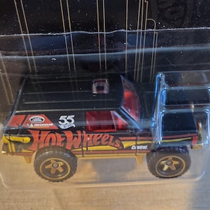 May include: A black and red Hot Wheels toy truck with gold and yellow accents. The truck has the number 55 on the side and the Hot Wheels logo. The wheels are gold.