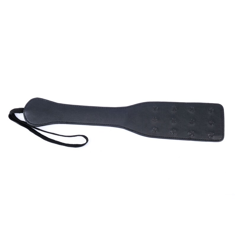 May include: A black leather paddle with a strap. The paddle has a textured surface.