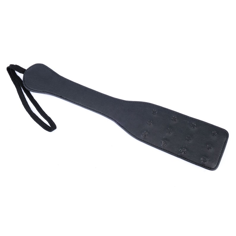 May include: A black leather paddle with a strap. The paddle has a textured surface with small raised dots.