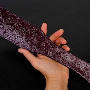 May include: A purple leather paddle with an embossed floral design. The paddle has a black cord attached to the end.