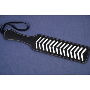 May include: A black leather paddle with white stitching in a chevron pattern. The paddle has a handle with a loop for hanging.