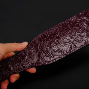 May include: A dark purple leather paddle with an intricate floral pattern embossed on the surface.