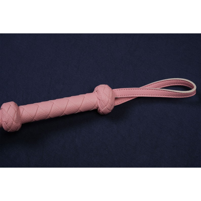 May include: A pink leather whip with a braided handle and a loop at the end.