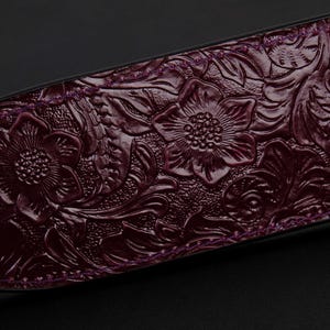 May include: A close-up of a dark purple leather paddle with an embossed floral design.