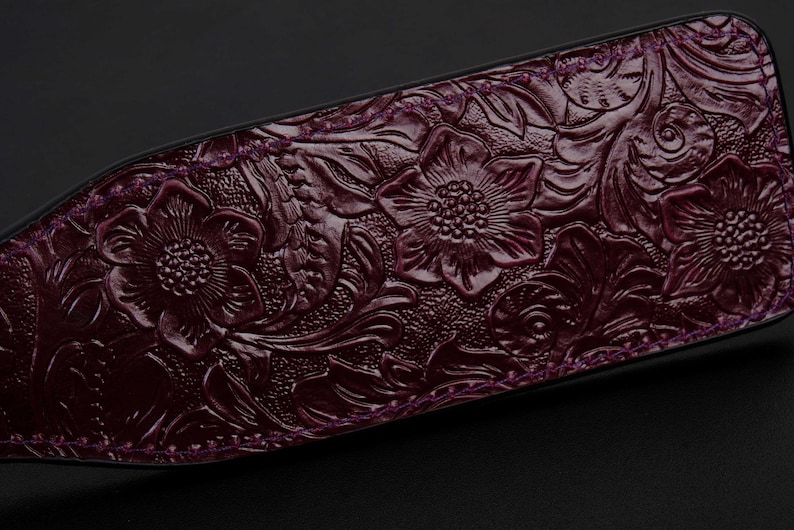 May include: A close-up of a dark purple leather paddle with an embossed floral design.