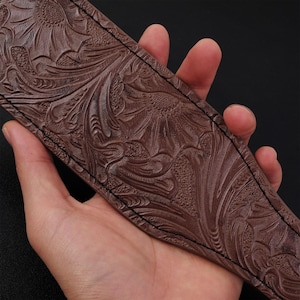 May include: A brown leather guitar strap with a floral embossed pattern. The strap has a stitched edge.