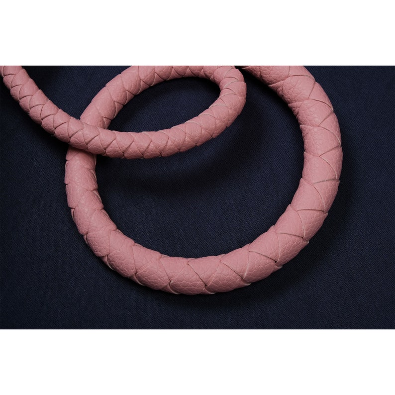 May include: Close-up of a pink braided leather strap. The strap is woven in a tight, intricate pattern.