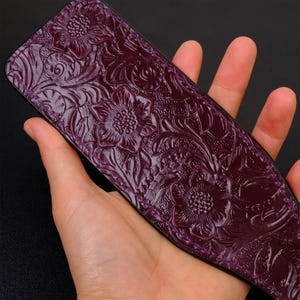 May include: A purple leather paddle with an embossed floral design. The paddle is held in a hand.