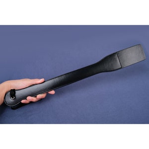 May include: A black leather paddle with a strap and a loop at the end.