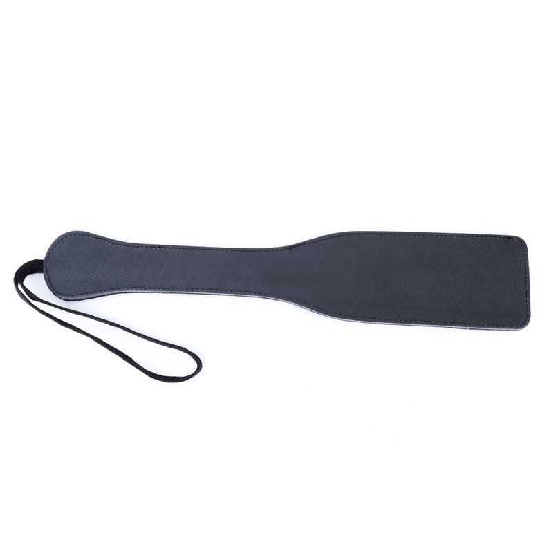 May include: A black leather paddle with a strap. The paddle is about 15 inches long and 4 inches wide.