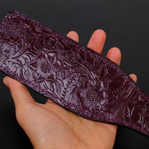 May include: A purple leather paddle with an embossed floral design. The paddle is held in a hand.