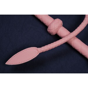 May include: A pink leather whip with a braided handle and a pointed tip.