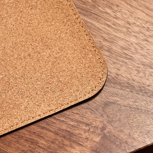 May include: A close-up of a brown cork desk mat with a stitched edge. The mat is on a wooden surface.