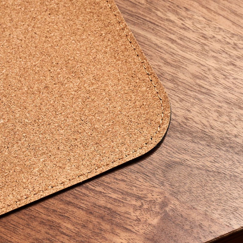 May include: A close-up of a brown cork desk mat with a stitched edge. The mat is on a wooden surface.