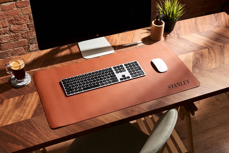 May include: A brown leather desk mat with a silver keyboard and white mouse. The mat has the name "STANLEY" embossed on it.