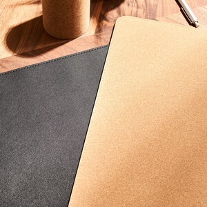 May include: A close-up of two desk mats, one black and one cork. The cork mat is textured and has a natural brown color. The black mat is smooth and has a subtle sheen.