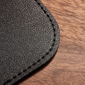 May include: Close-up of a black leather patch with a stitched edge. The patch is on a brown wooden surface.
