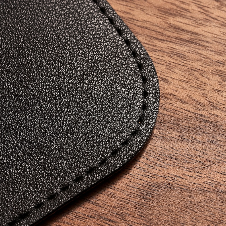 May include: Close-up of a black leather patch with a stitched edge. The patch is on a brown wooden surface.