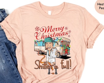 May include: A heather peach t-shirt with a Christmas-themed graphic of a man in a white robe standing next to a camper van with the text "Merry Christmas Shitter's Full!"