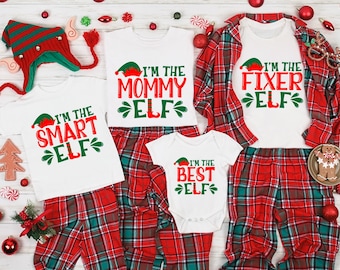 Pode incluir: Um conjunto de quatro pijamas de Natal combinando com calças xadrez vermelhas e verdes e camisas brancas com o texto "Eu sou o duende mamãe", "Eu sou o duende inteligente", "Eu sou o duende consertador" e "Eu sou o melhor duende".