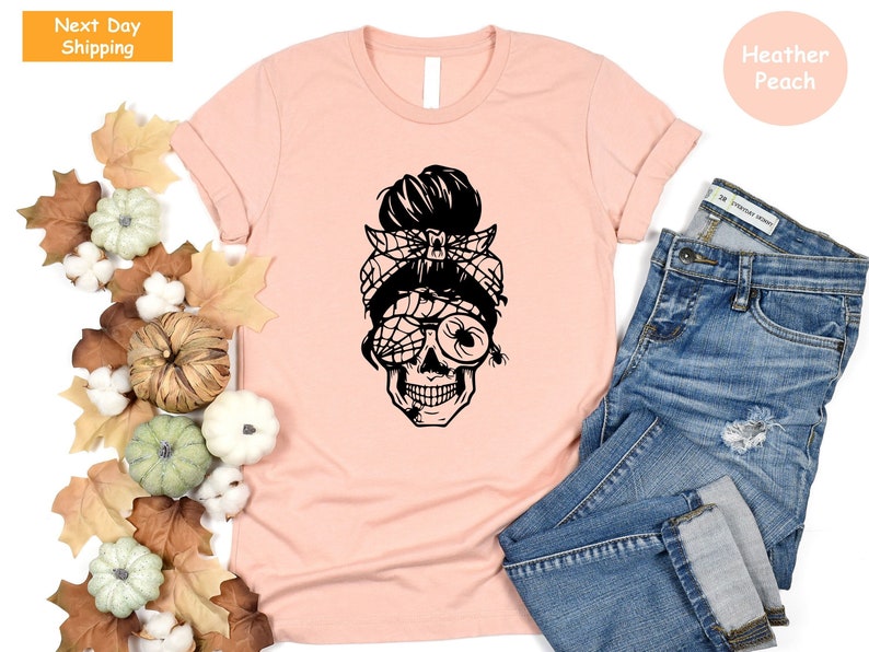 May include: A pink t-shirt featuring a black graphic of a skull with a messy bun and spiderweb sunglasses. The text "Heather Peach" is visible in the top right corner of the image.
