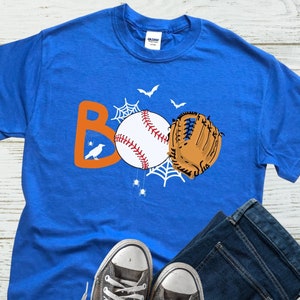 May include: A royal blue t-shirt with an orange "BOO" graphic featuring a baseball, a baseball glove, and a spider web. The graphic also includes a small black bird.