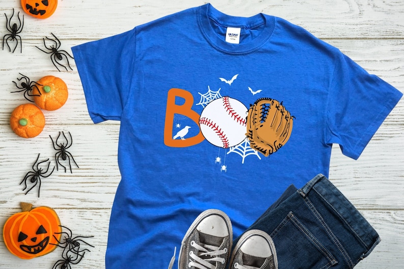 May include: A royal blue t-shirt with an orange "BOO" graphic featuring a baseball, a baseball glove, and a spider web. The graphic also includes a small black bird.