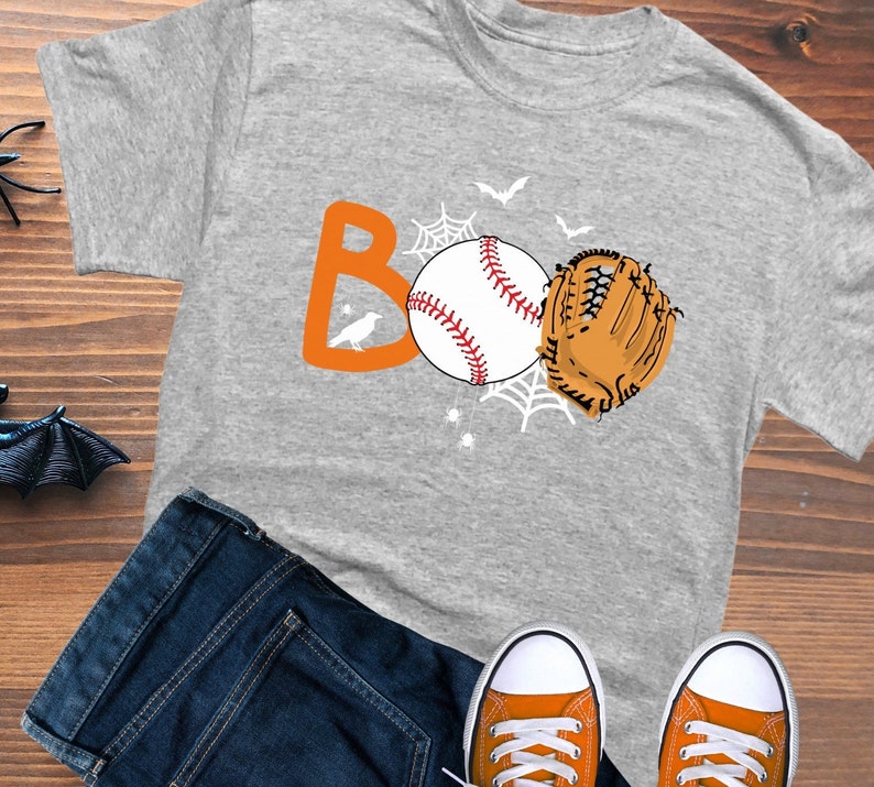 May include: Gray t-shirt with an orange "BOO" graphic featuring a baseball, a baseball glove, and bats. The graphic also includes a spider web and a small bird.