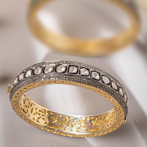Può includere: Un braccialetto rigido in oro con un design delicato e intricato. Il braccialetto è adornato con piccoli diamanti rotondi e un bordo in smalto nero.