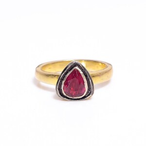 Op de afbeelding: Een gouden ring met een rode edelsteen gezet in een zilveren zetting. De ring is simpel en elegant.