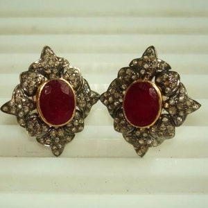 May include: A pair of silver earrings with a red gemstone set in a floral design. The earrings are adorned with small diamonds.