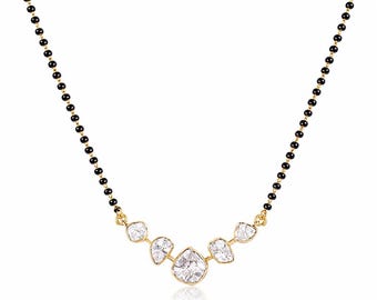 May include: A necklace featuring a chain of small black beads and a central gold-toned pendant. The pendant consists of five irregular, clear, faceted stones set in gold-toned metal, arranged in a curved, symmetrical V-shape design.