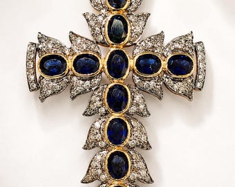 May include: A cross-shaped pendant featuring a central vertical and horizontal arrangement of oval-cut deep blue sapphires set in yellow gold, surrounded by intricate silver-toned metal leaf-shaped accents encrusted with small clear white diamonds.