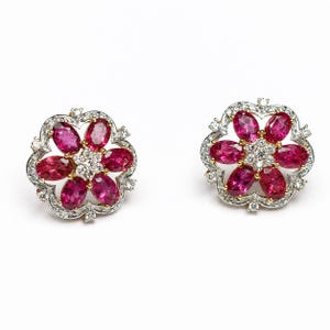 May include: A pair of floral-shaped stud earrings crafted in silver and gold, each featuring six oval-cut vibrant pink gemstones arranged in a petal pattern around a central cluster of small, clear, round-cut white diamonds.