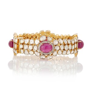 Op de afbeelding: Een gouden armband met een ontwerp van robijnen en diamanten. De armband is gemaakt van goud en heeft een rij robijnen en diamanten.